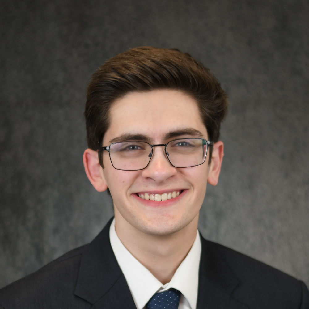 A headshot of a handsome, professional-looking young man wearing a suit, a tie, and a charming smile.